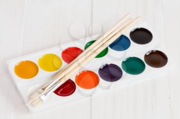 Watercolor paints with set of paint brushes on white wooden background