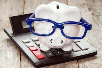Piggy bank in glasses with calculator on the wooden background