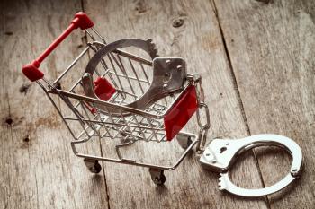 Shopping cart and handcuffs on wooden background