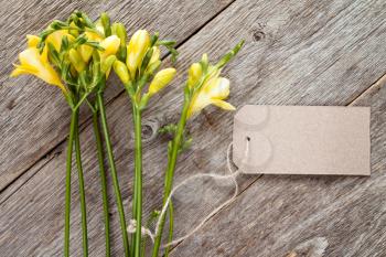 Yellow freesia flowers with blank tag on old wooden background