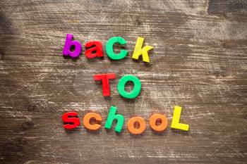   Sentence Back to school in colorful plastic letters over dark wooden background