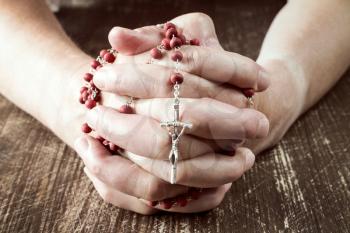 Praying hands holding red rosary with  cross 