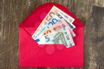 Red envelope with Euro bills over wooden background