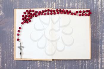 Open book and catholic rosary on wooden background