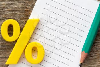 Note paper with pencil and yellow plastic percentage sign
