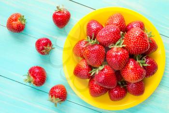 Yellow plate with red strawberries on blue wooden background