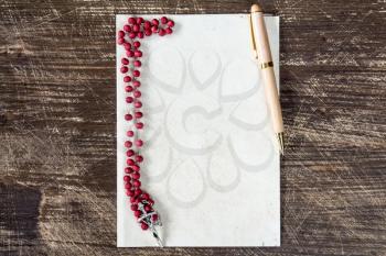 Catholic rosary and pen on blank paper sheet with copy-space