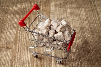 Shopping cart full of brown cane sugar on wooden background