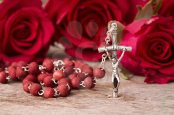 Silver crucifix and red roses on wooden background