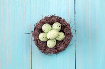 Nest with painted eggs on wooden background. Top view.