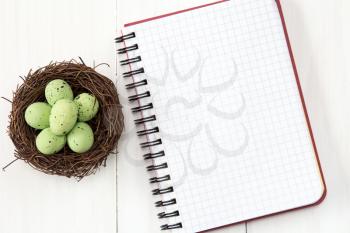 Nest with painted eggs and blank notebook for copy-space