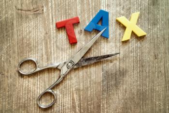 Cut of tax Concept. Scissors and the colorful plastic alphabet on wooden background. 