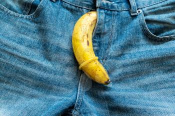 Banana in condom protruding from blue jeans