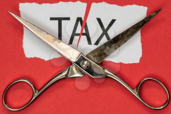  Scissors and printed paper with the word tax on it cut in half. Tax cuts and saving money concept