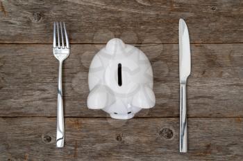  Savings consumer concept. Piggy bank with fork and knife