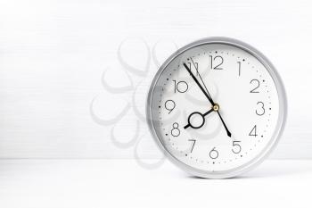 Silver wall clock on white wooden desk. Copy-space.