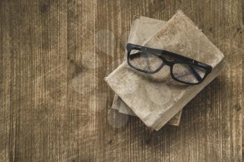 Old books with eyeglasses on wooden table,top view
