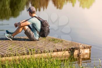 Back view of man with backpack sitting on a wooden pier