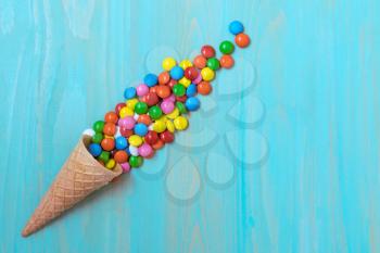 Waffle horn with colored candy on a blue wood background. Top view, copy-space.