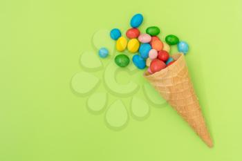  Waffle horn with colored candy on green background. Top view, copy-space