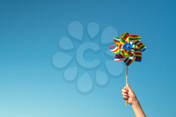 Child holds colorful pinwheel on blue sky background