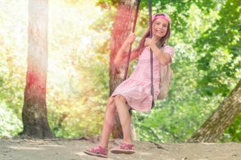Cute little girl having fun on a swing  on warm and sunny day outdoors. Active summer leisure for kids.
