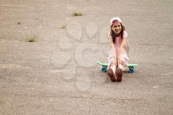 Little girl child sits on the skate board 