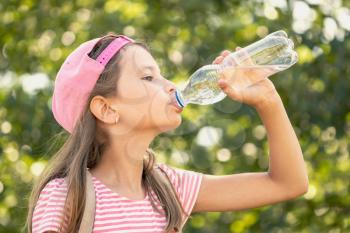 Thirsty child girl drinking water in a park 