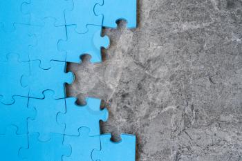 Unfinished blue jigsaw puzzle pieces on stone background. Copy-space