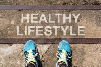 Text HEALTHY LIFESTYLE written on concrete stairs with man legs in sneakers, view from above
