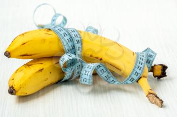 Closeup view of bananas and measuring tape on white wooden background.Healthy eating or dieting concept
