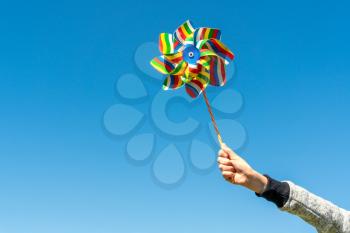 Child's hand with colorful pinwheel  on blue sky background