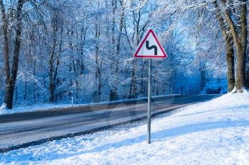 Winter driving concept - curvy winter road with warning sign