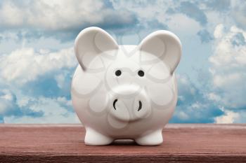 White piggy bank with cloudy sky background. Saving or investment concept