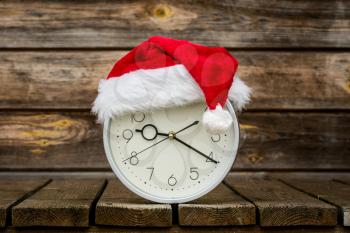 Christmas time - wall clock with Santa hat on the wheatered wood background