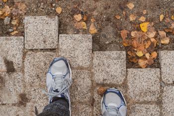 Unfinished pavement with fallen leaves and man's feet. Depressed emotions or crisis concept