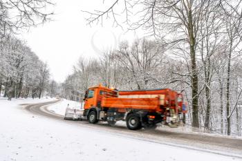 Snow ploughing truck cleans the country road leading through the  forest during a snowfall. Dangerous road conditions.