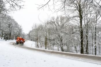 Snow ploughing truck cleans the road leading through the forest during a snowfall