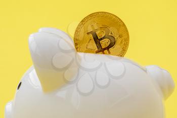 Piggy bank with bitcoin coin on yellow background. Close-up view.