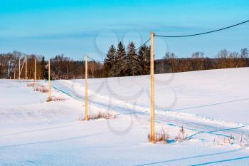 Empty rural road, snowy winter landscape, electricity poles.