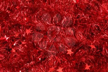 Scattered shiny festive tinsel of red color. Red Christmas background.