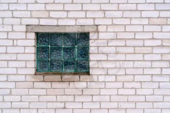 Squares of corrugated green glass in the white brick wall