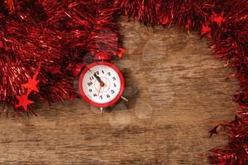 Counting last minutes before Christmas or New Year. Countdown to midnight. Red alarm clock lying on table with red garland and tinsel close up. Copy space.
