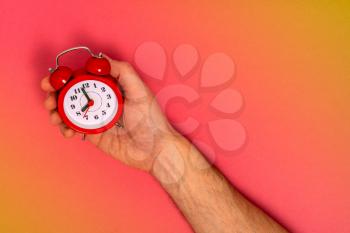 Man holding red alarm clock in one hand on colorful background with copy space