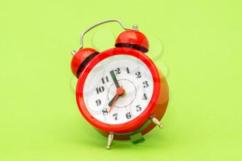 Vintage alarm clock falling on the green background. Red alarm clock showing 8 o'clock in a morning.