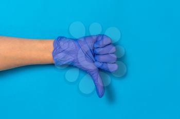 Female hand in medical glove shows gesture thumb down or dislike