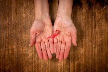 Female hands holding pink ribbon on the wooden background.  Supporting symbol of breast cancer awareness.