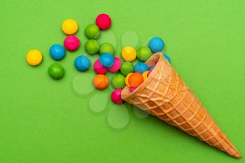 Waffle horn with many colorful candies on green background