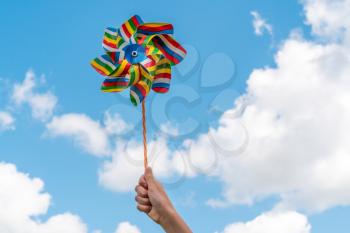 Front view of colourful pinwheel windmill on a hand, isolated on sky background.