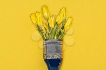 Creative spring concept made with paint brush and yellow tulip flowers. 